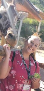 woman smiles for camera while feeding giraffe